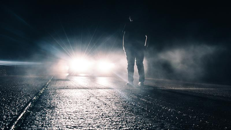 Pedestrian standing in front of car with high beams on.