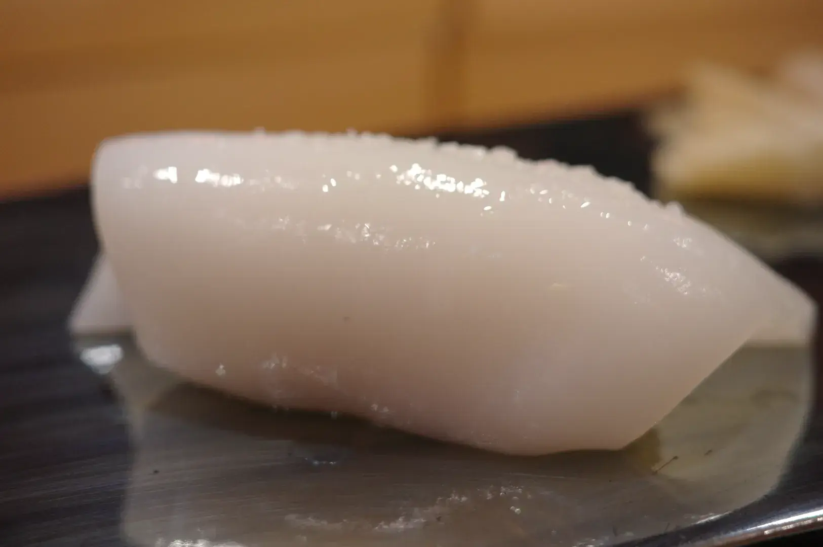 A piece of sushi, likely made with translucent white fish or seafood, resting on a plate.