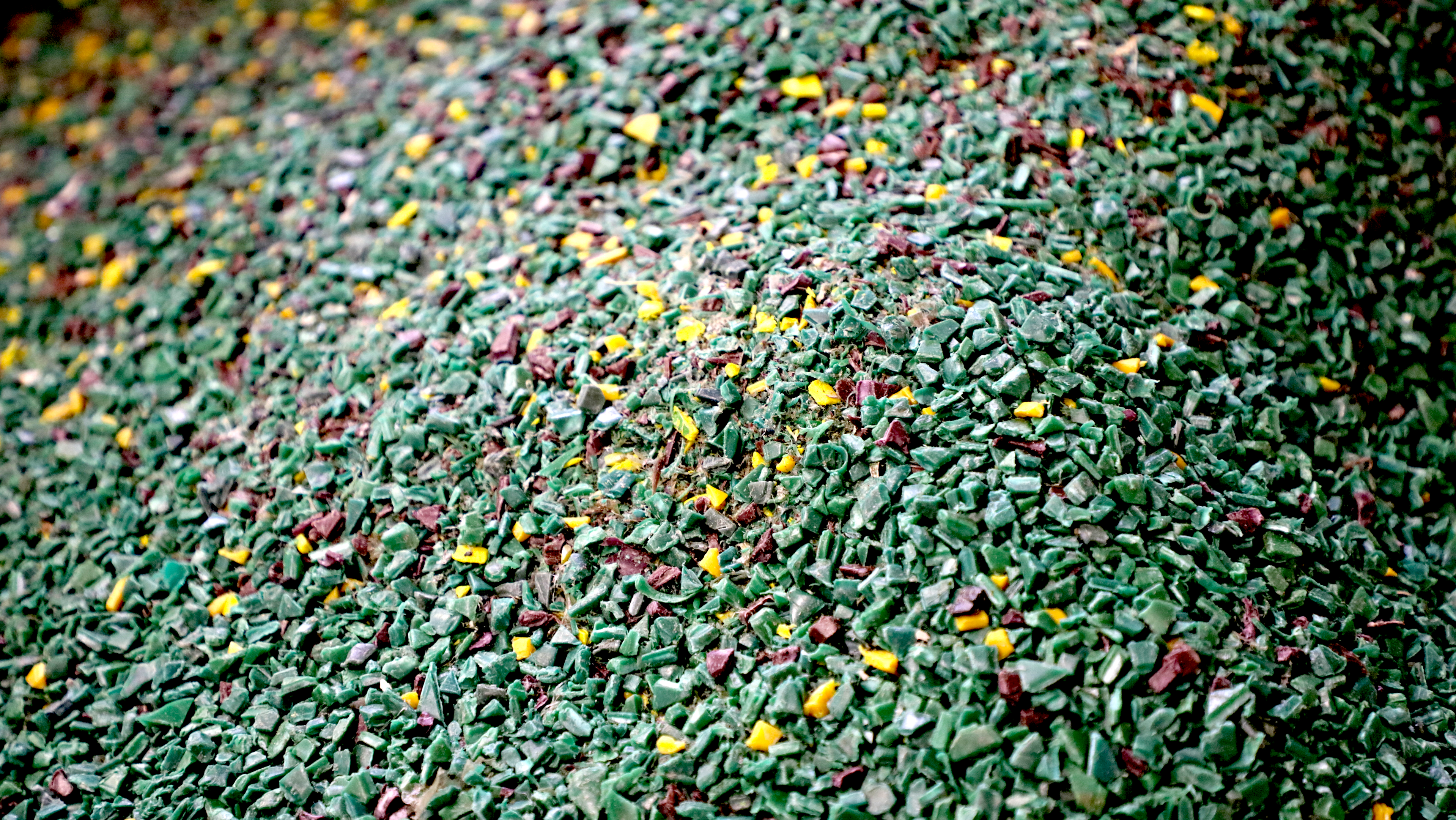 The image features a vibrant assortment of recycled plastic pellets and regrind material scattered across an industrial surface, highlighting the raw materials used in the plastic injection molding process. These colorful plastics are essential for manufacturing plastic parts and components, showcasing the versatility and efficiency of modern industrial processes.