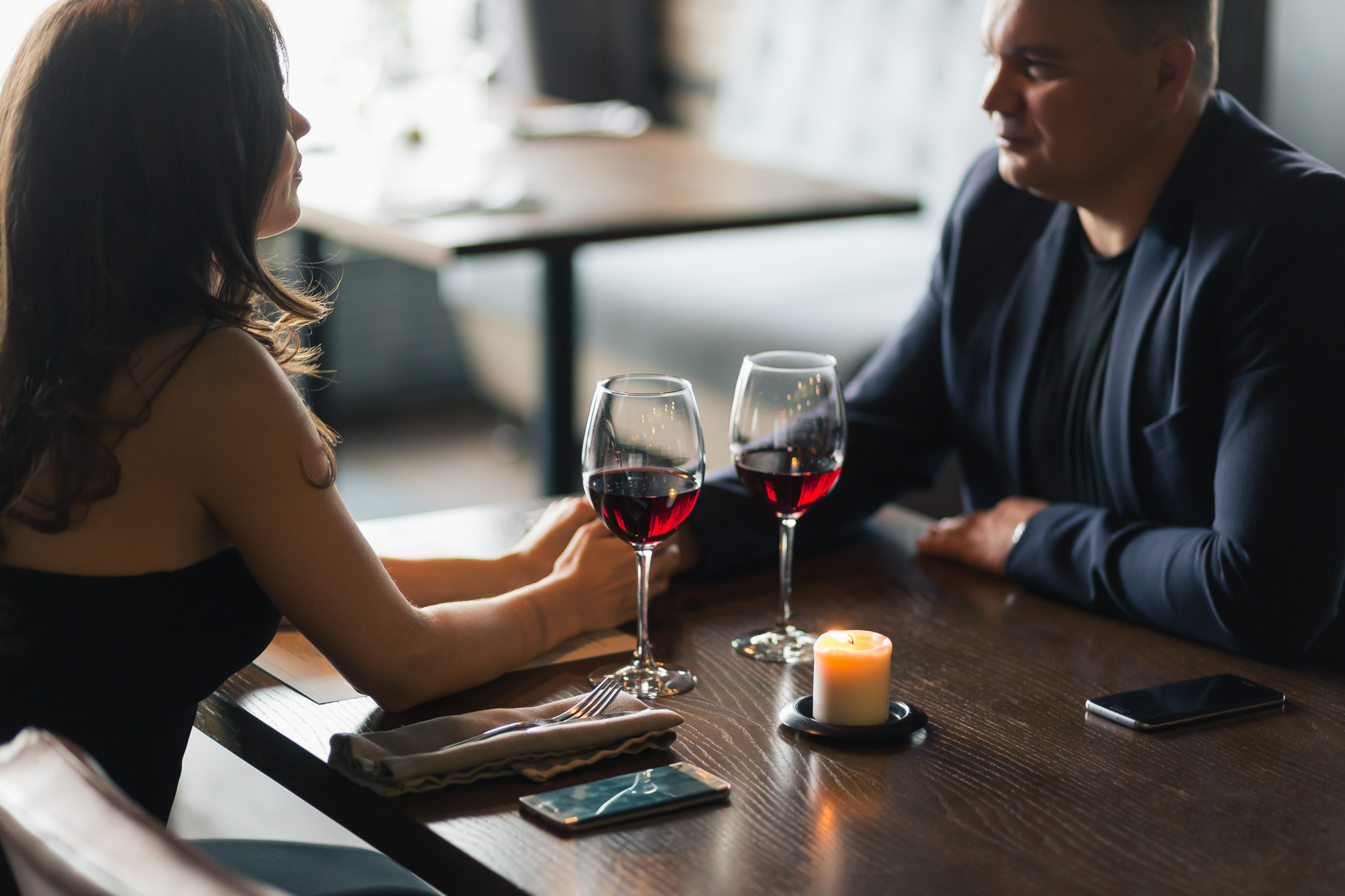 Man and woman sitting at a table holding hands with glasses of red wine.