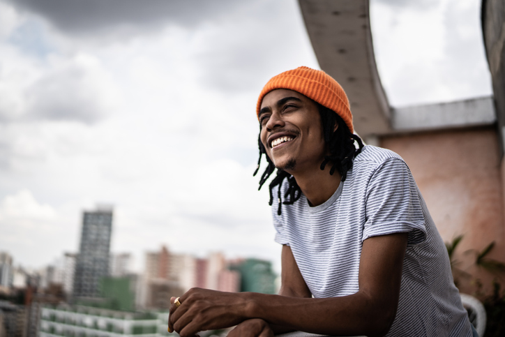 Young African American man in an orange cap looking out over the city from a balcony.