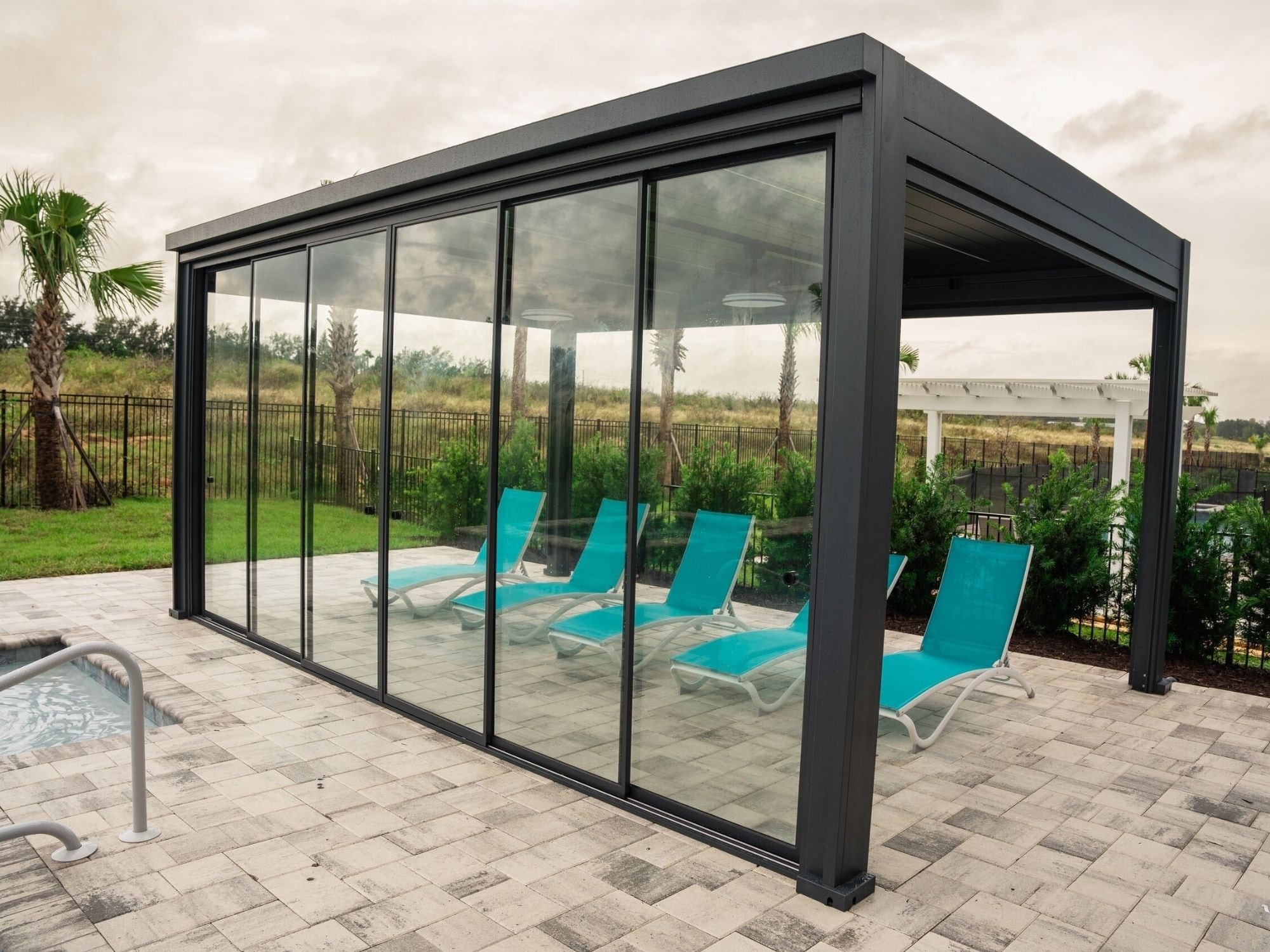 Une pergola bioclimatique haut de gamme est installée sur une terrasse, au bord d'une piscine, avec des lames orientables intégrant un éclairage LED. Cet espace extérieur élégant offre une protection contre le soleil et la pluie, tout en apportant confort et style à votre jardin.