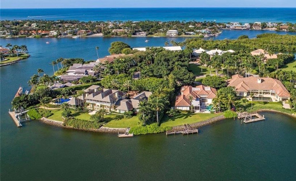 This image depicts a stunning waterfront estate in the prestigious Port Royal neighborhood, featuring an enormous infinity pool that seamlessly blends with the serene views of Naples Bay at sunset. The luxurious property showcases expansive outdoor living spaces and epitomizes beachfront luxury living, offering a tranquil retreat with private beach access.