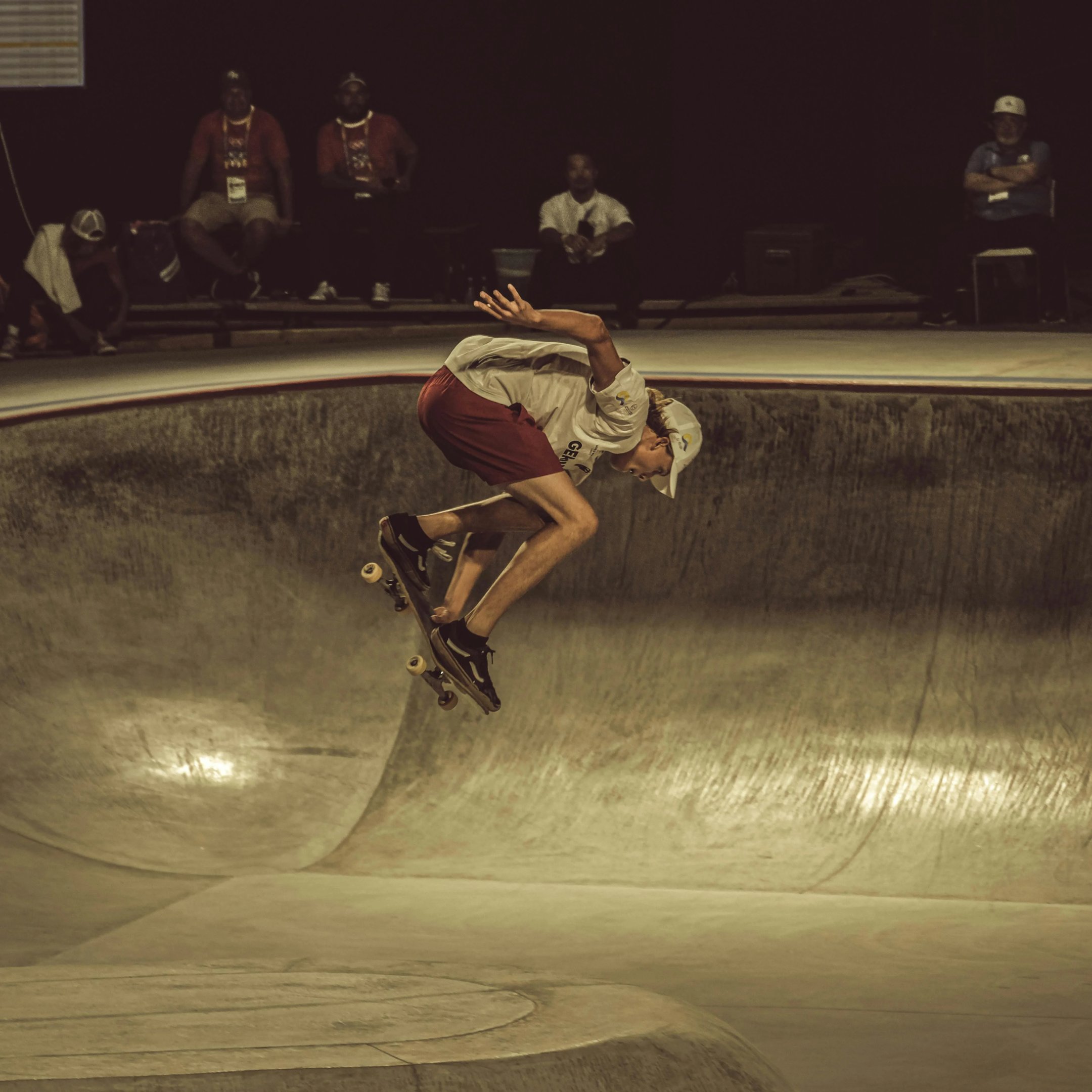 "Skateboarder performing aerial trick in concrete bowl during skatepark event, surrounded by spectators."