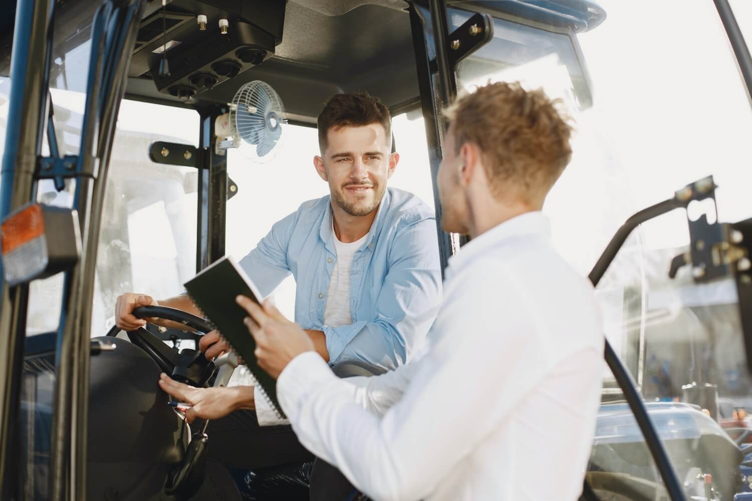 a man sitting in a forklift truck discussing the risk management policy with a manager next to him