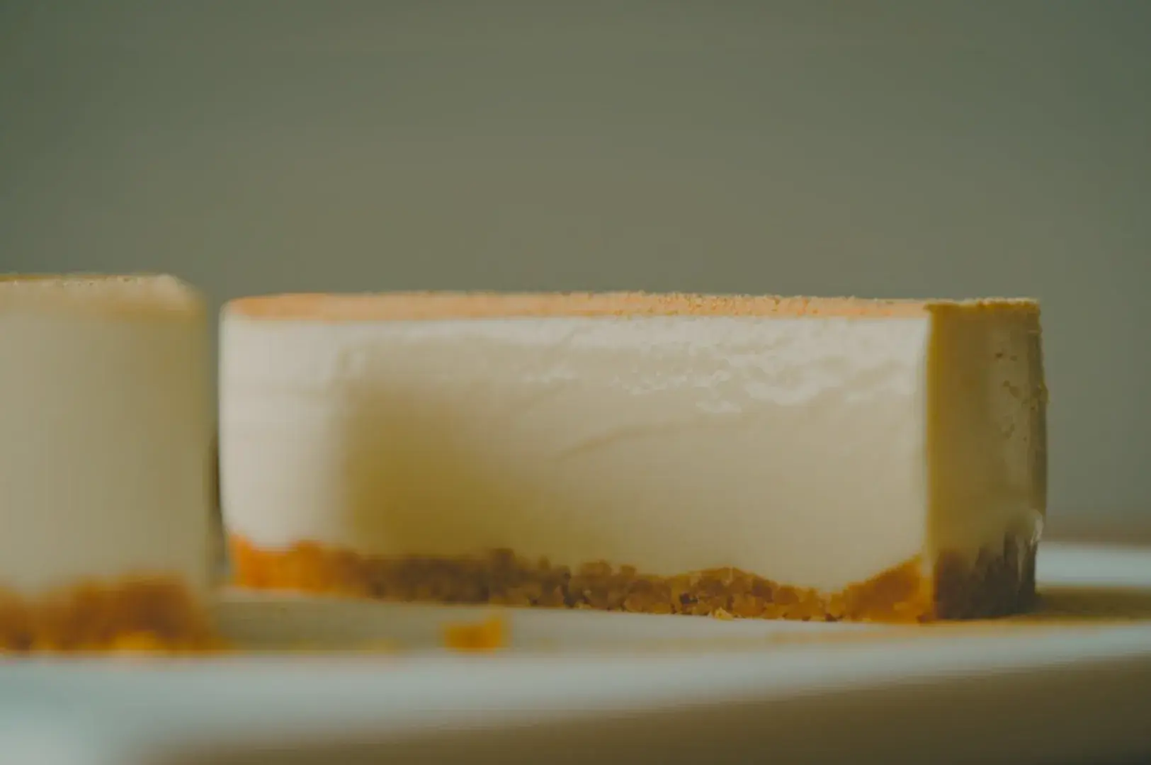 A close-up of a slice of cheesecake showing a smooth, creamy layer on top with a crumbly crust at the bottom.