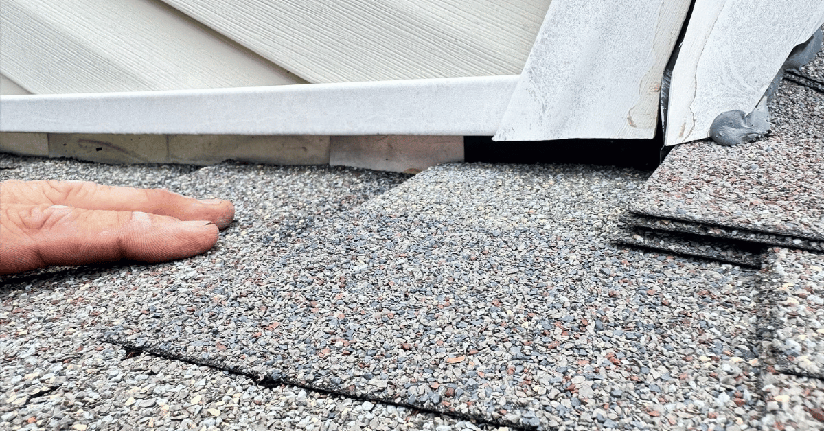 Missing asphalt shingles at flashing near a wall, exposing underlayment and showing heat-related roof damage.