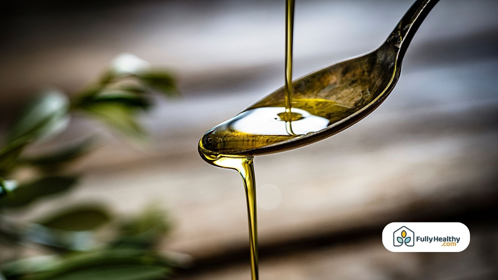 Olive oil pouring onto a spoon with blurred olive leaves background