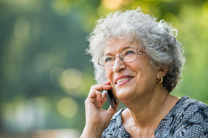 Older woman with gray hair smiling and talking on a cell phone. 
