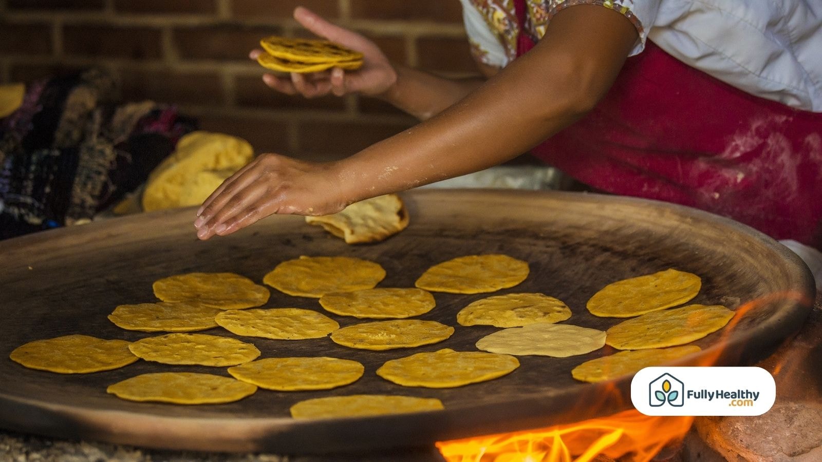 Hand placing corn tortillas on traditional round clay comal