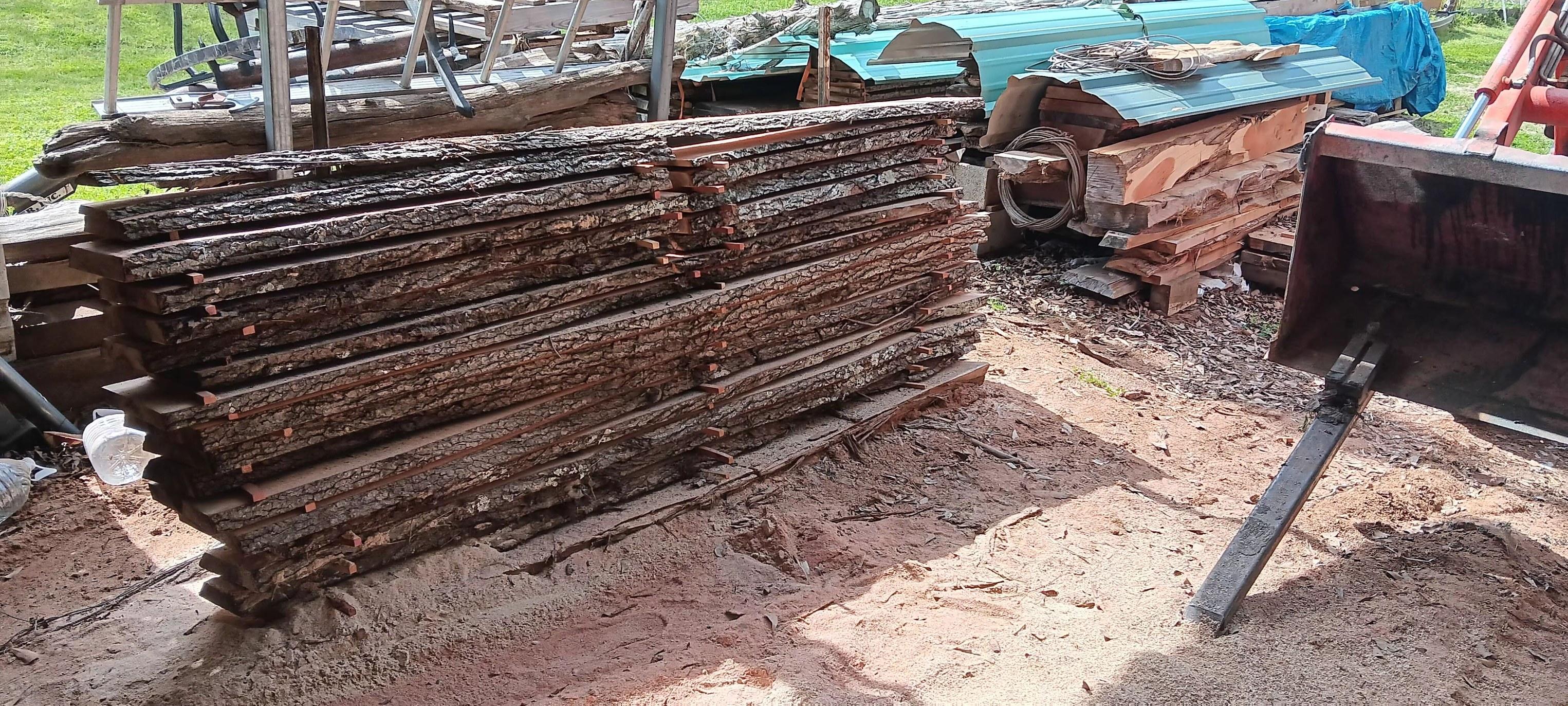 Une pile de planches à bords naturels, marquées d'autocollants, posées à l'extérieur.