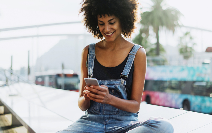 Pretty young woman in denim overalls sending a text. 