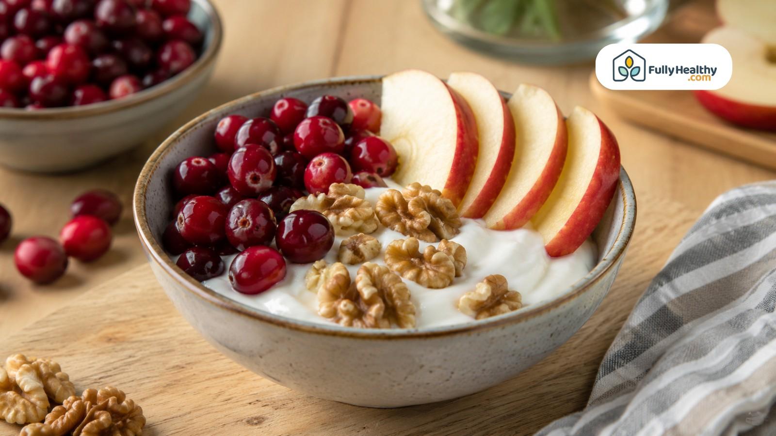 Plain yogurt topped with cranberries, apple slices, and walnuts on wooden table