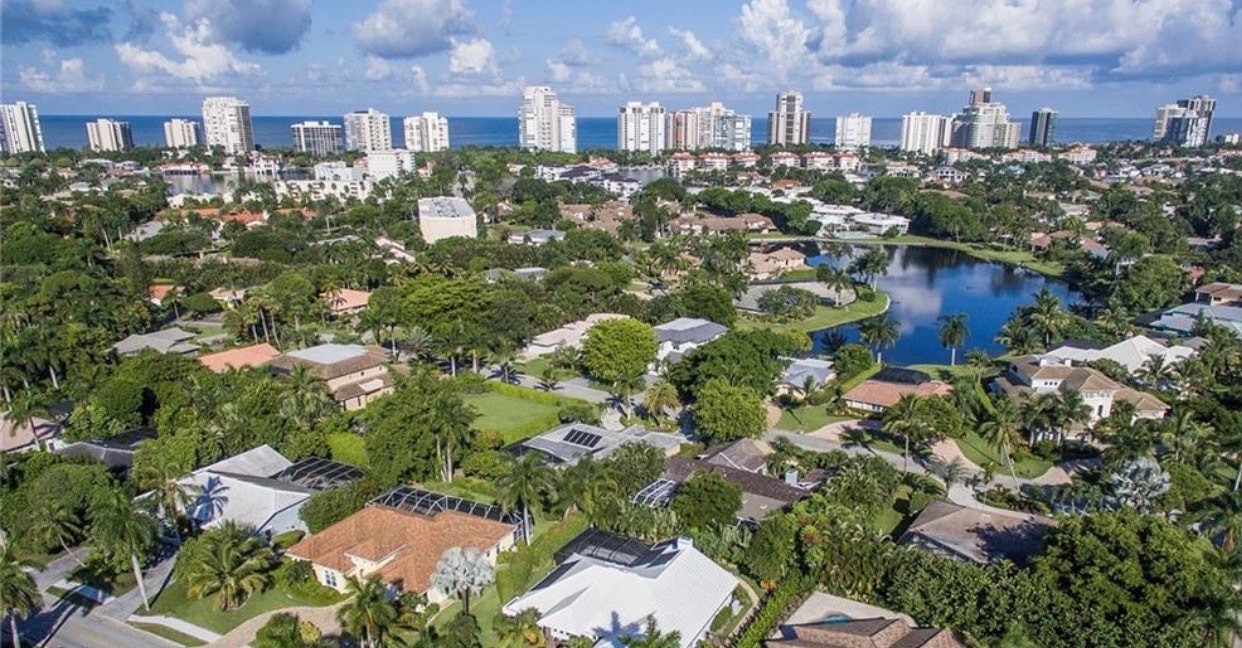 A stunning estate home nestled in the prestigious Pine Ridge community, showcasing sprawling grounds adorned with towering palm trees and a breathtaking resort-style pool. This luxurious residence features seamless indoor-outdoor living, with an expansive sitting room and outdoor living spaces perfect for relaxed gatherings.