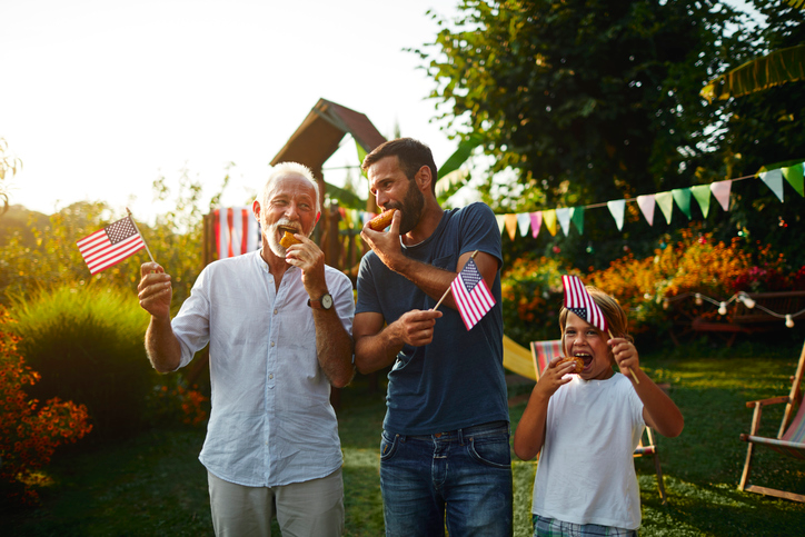 Grandpa, dad, and son enjoying hotdogs at a July 4th party.