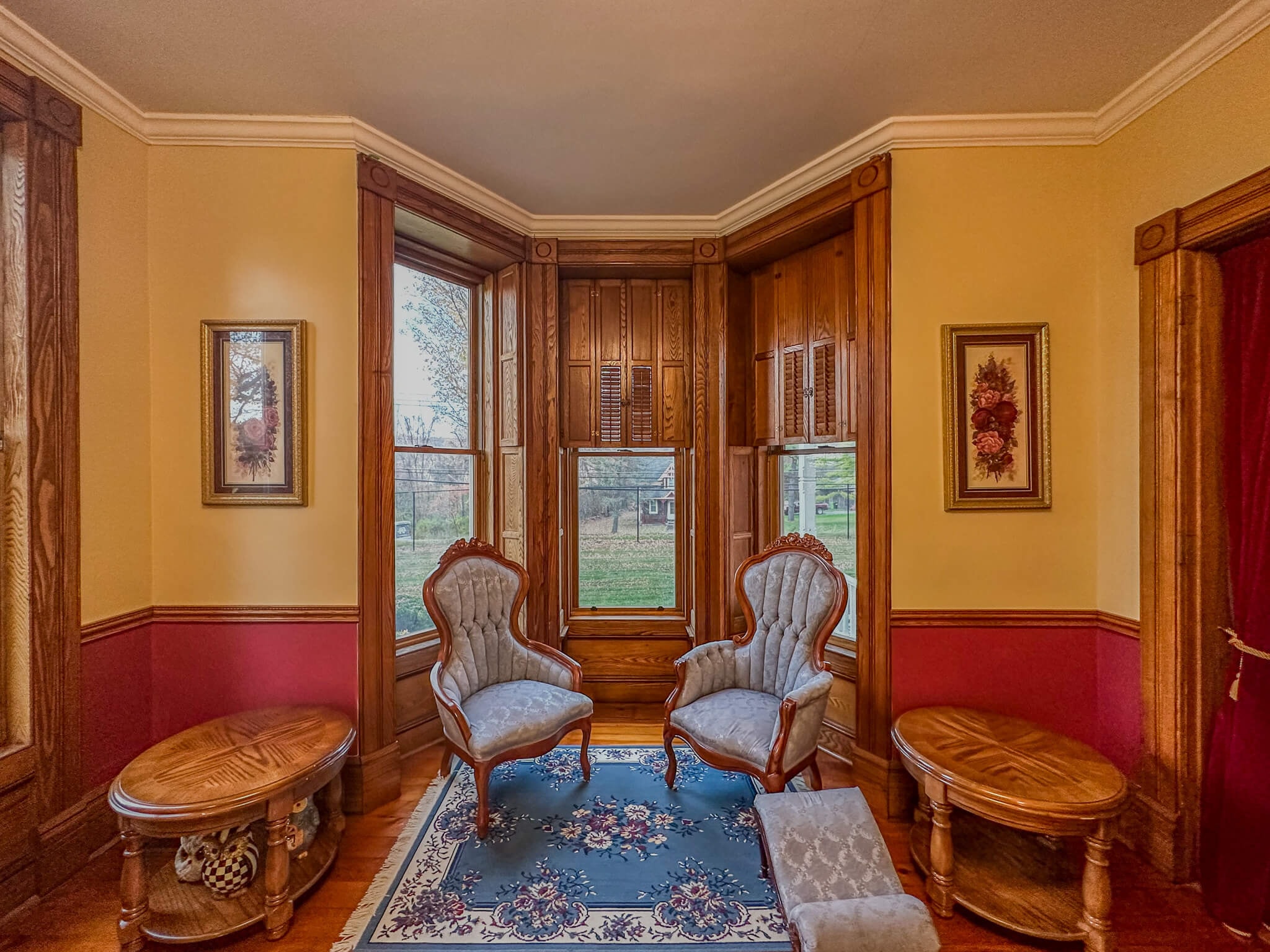 Interior view of a historic bay window sitting area in a restored Fayetteville, NY home. Features newly installed Andersen windows by McClurg Remodeling, surrounded by original wood trim and period furnishings.