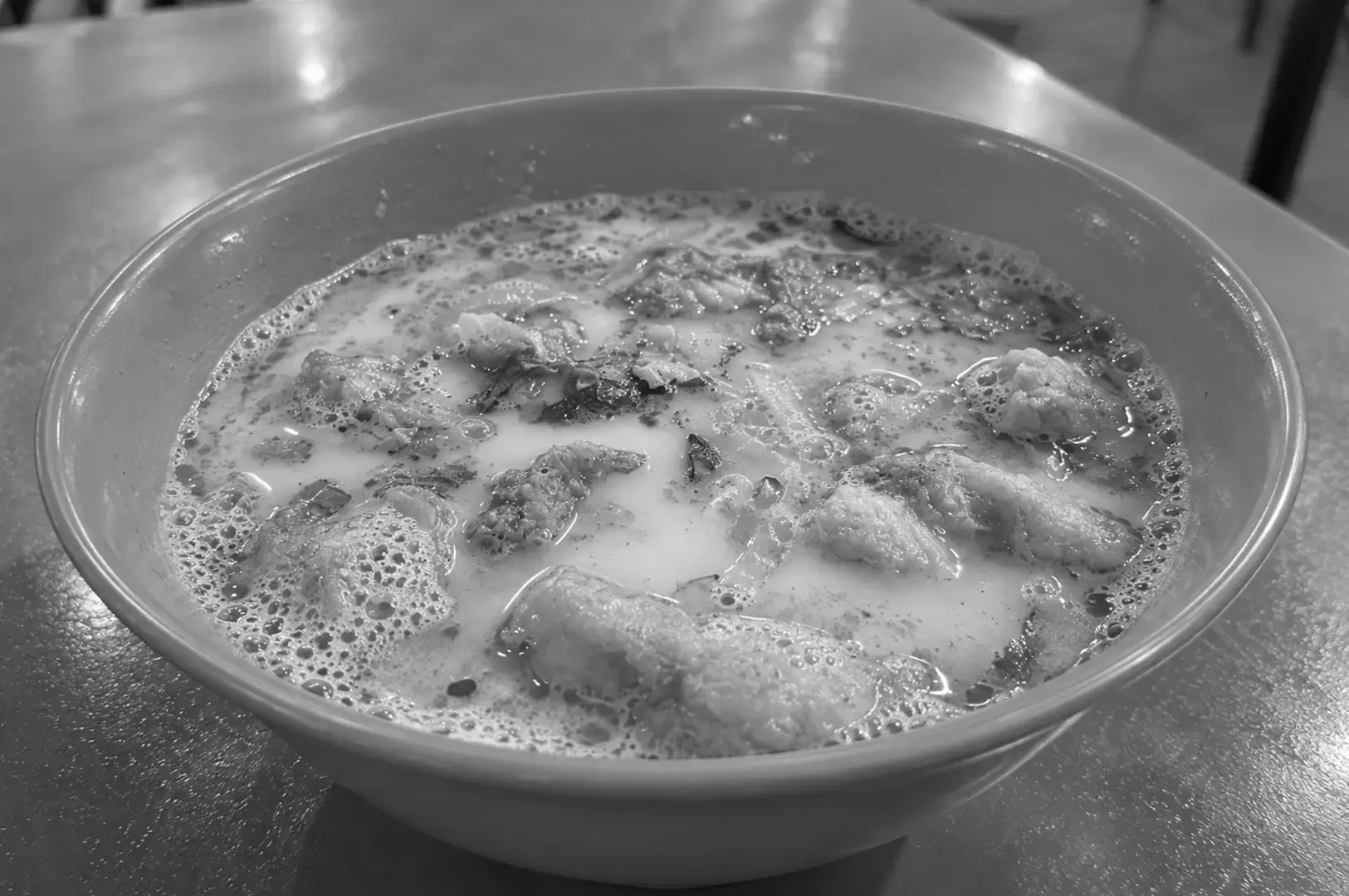 A bowl of Fried Fish Soup featuring crispy fried fish pieces, herbs, and ingredients in a creamy, milky broth.