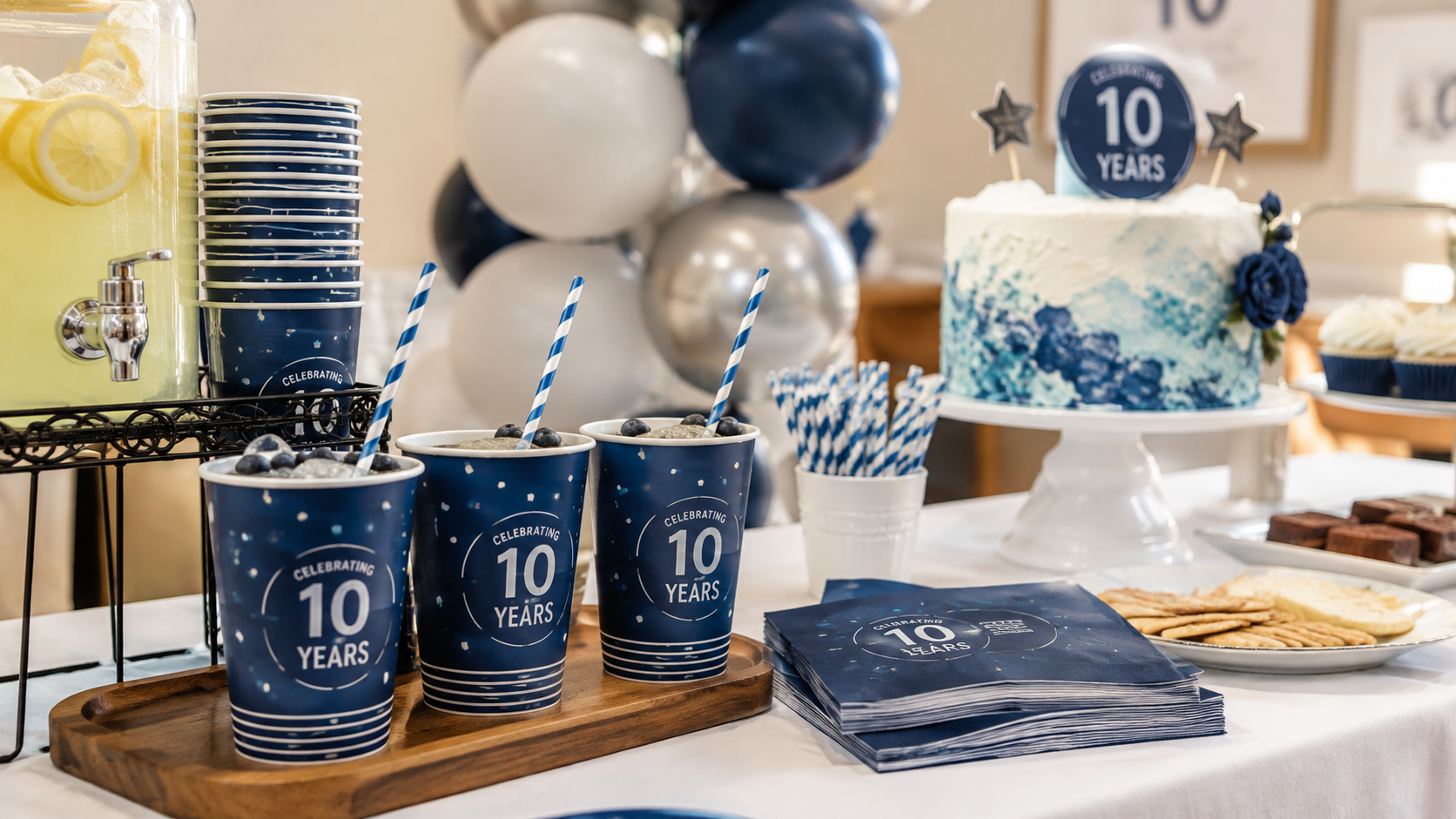 Custom party cups arranged beside a company anniversary cake, balloons, straws, and napkins