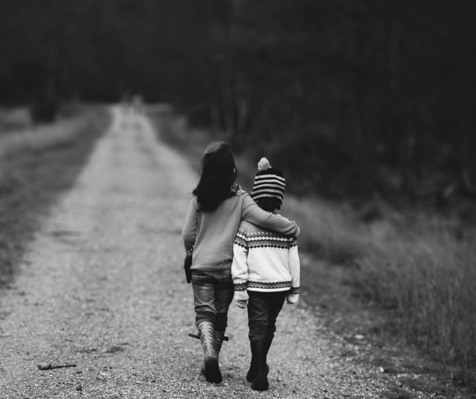 two kids walk arm in arm down a road