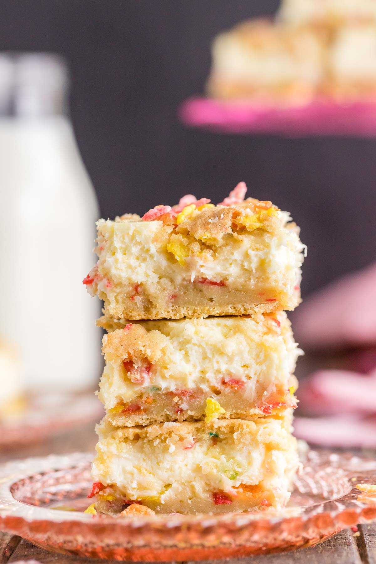 three fruity pebble cheesecake bars stacked on a pink plate