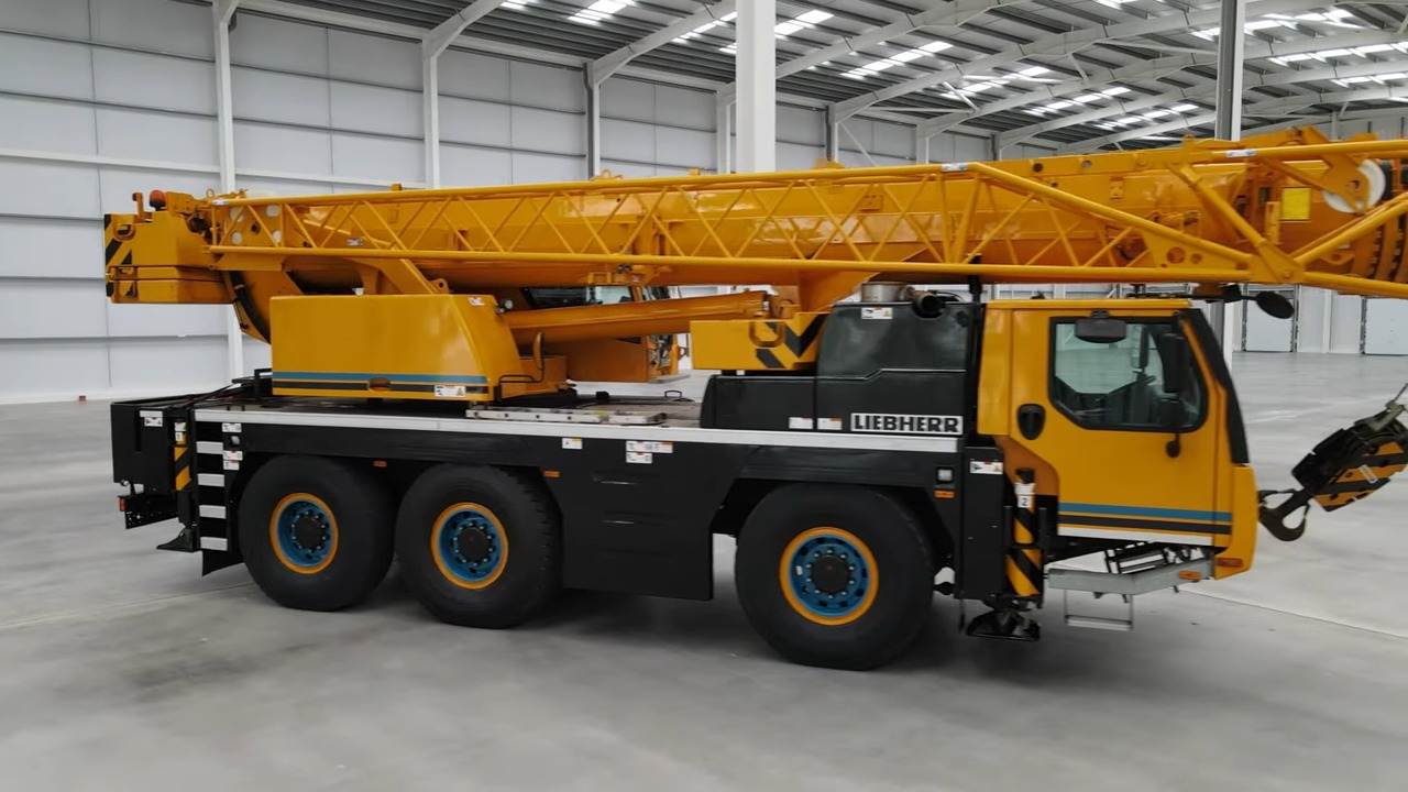 Yellow and black Liebherr mobile crane parked inside a clean, spacious industrial warehouse with reflective floor