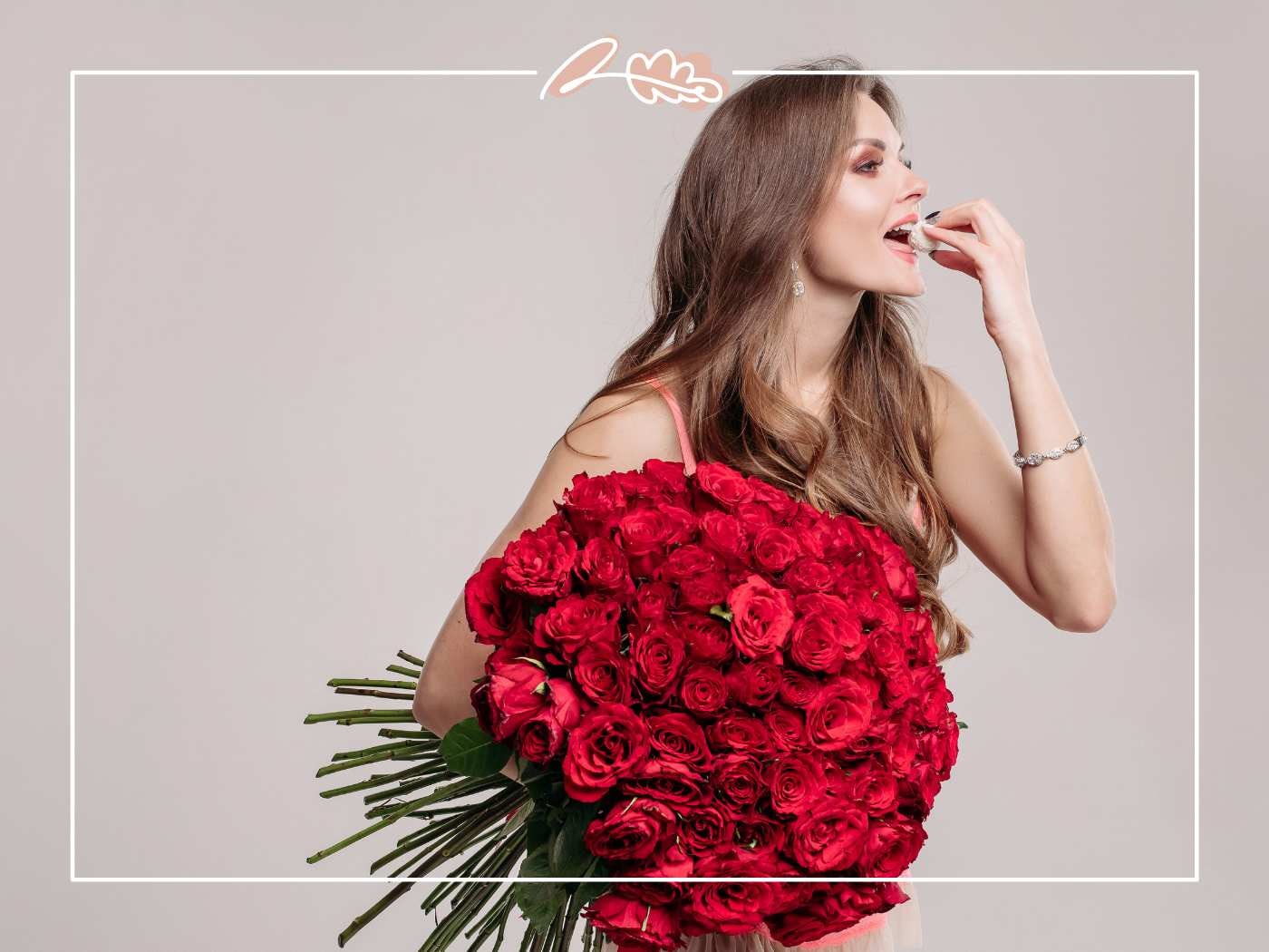 Woman in pink carries an oversized bouquet of red roses, nibbling a sweet, with Fabulous Flowers border.