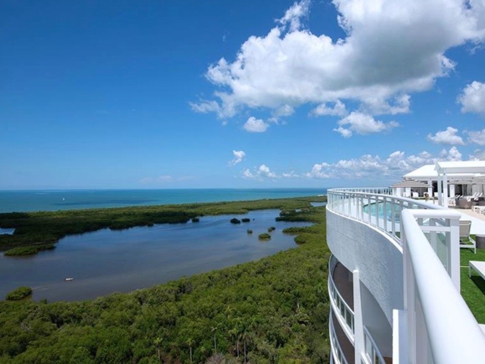 The image features a stunning rooftop infinity pool that overlooks the Gulf of Mexico, surrounded by modern lounge areas perfect for relaxation. As the sun sets, the scene captures the essence of luxury coastal living in the prestigious Kalea Bay community, highlighting breathtaking views and a sophisticated ambiance.