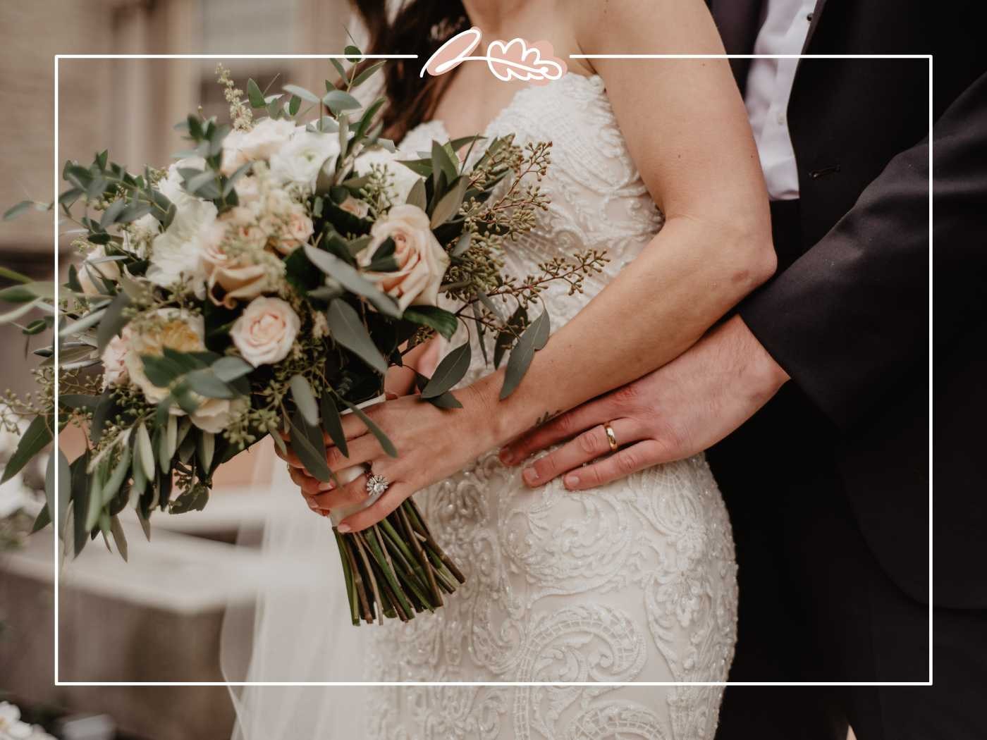 The bride and groom embracing, the bride holding a stunning bouquet of white and blush roses with greenery. Fabulous Flowers and Gifts.