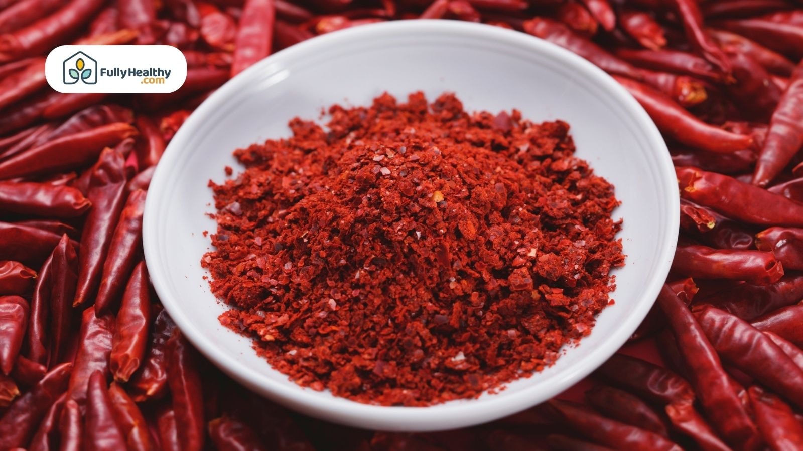 A bowl of finely ground red chili powder surrounded by dried whole chili peppers