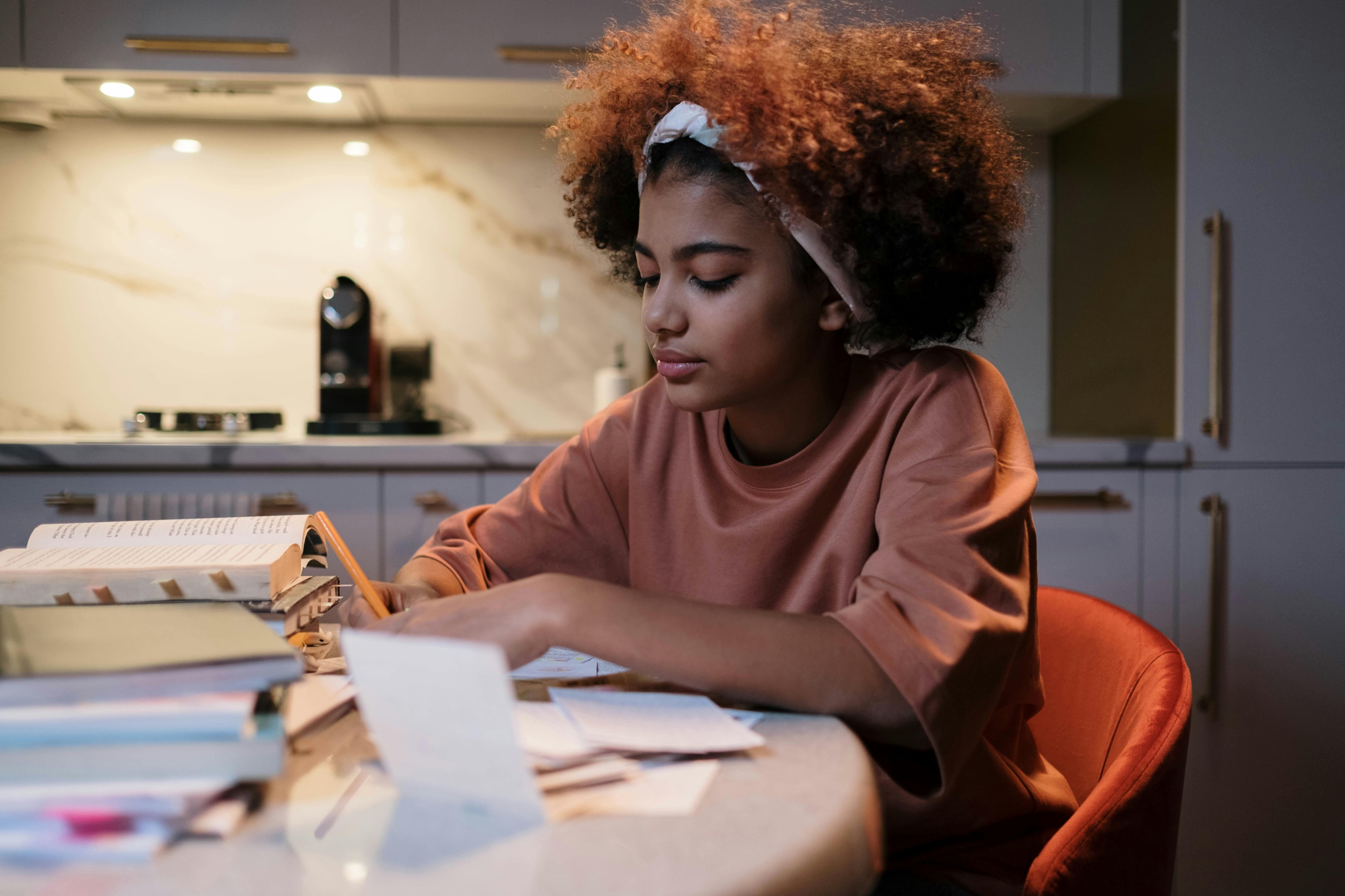 Girl writing in books sitting in the kitchen