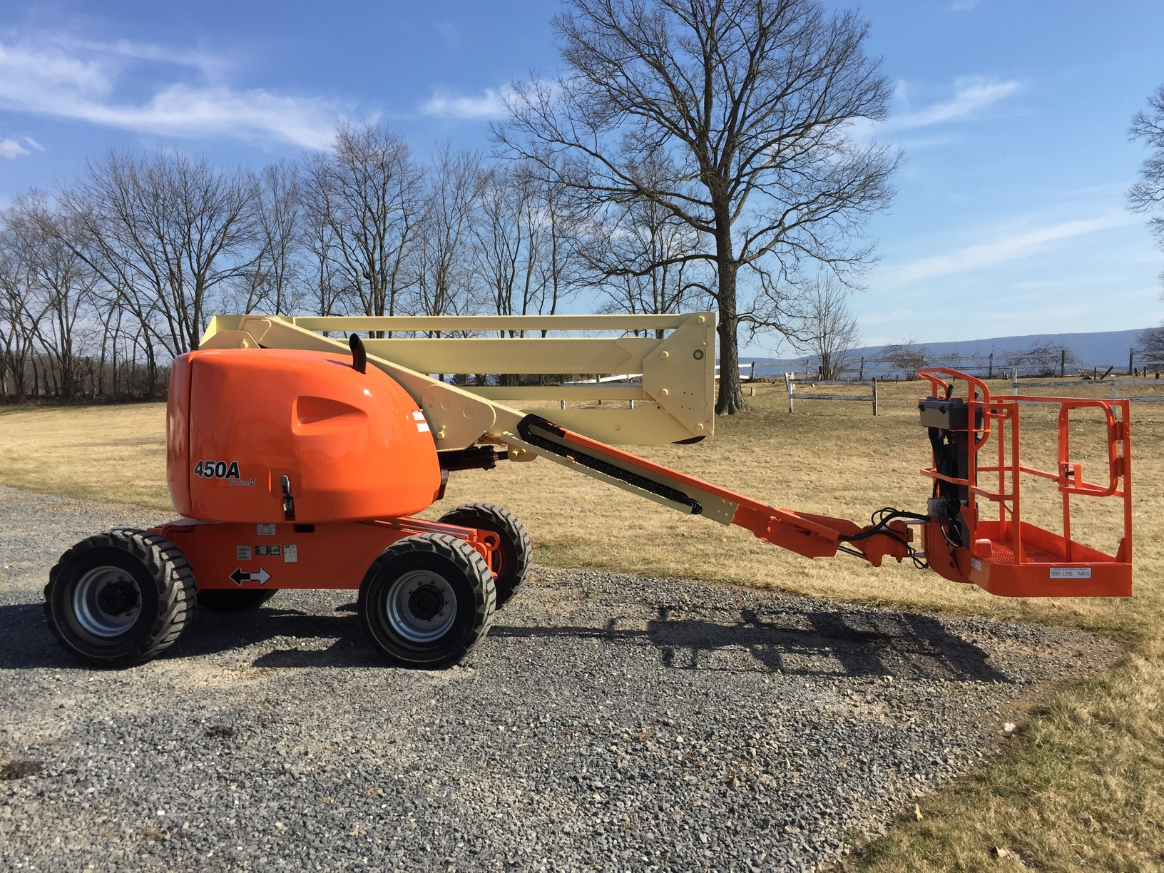 Orange JLG 450A articulating boom lift on a clear day with scenic countryside backdrop