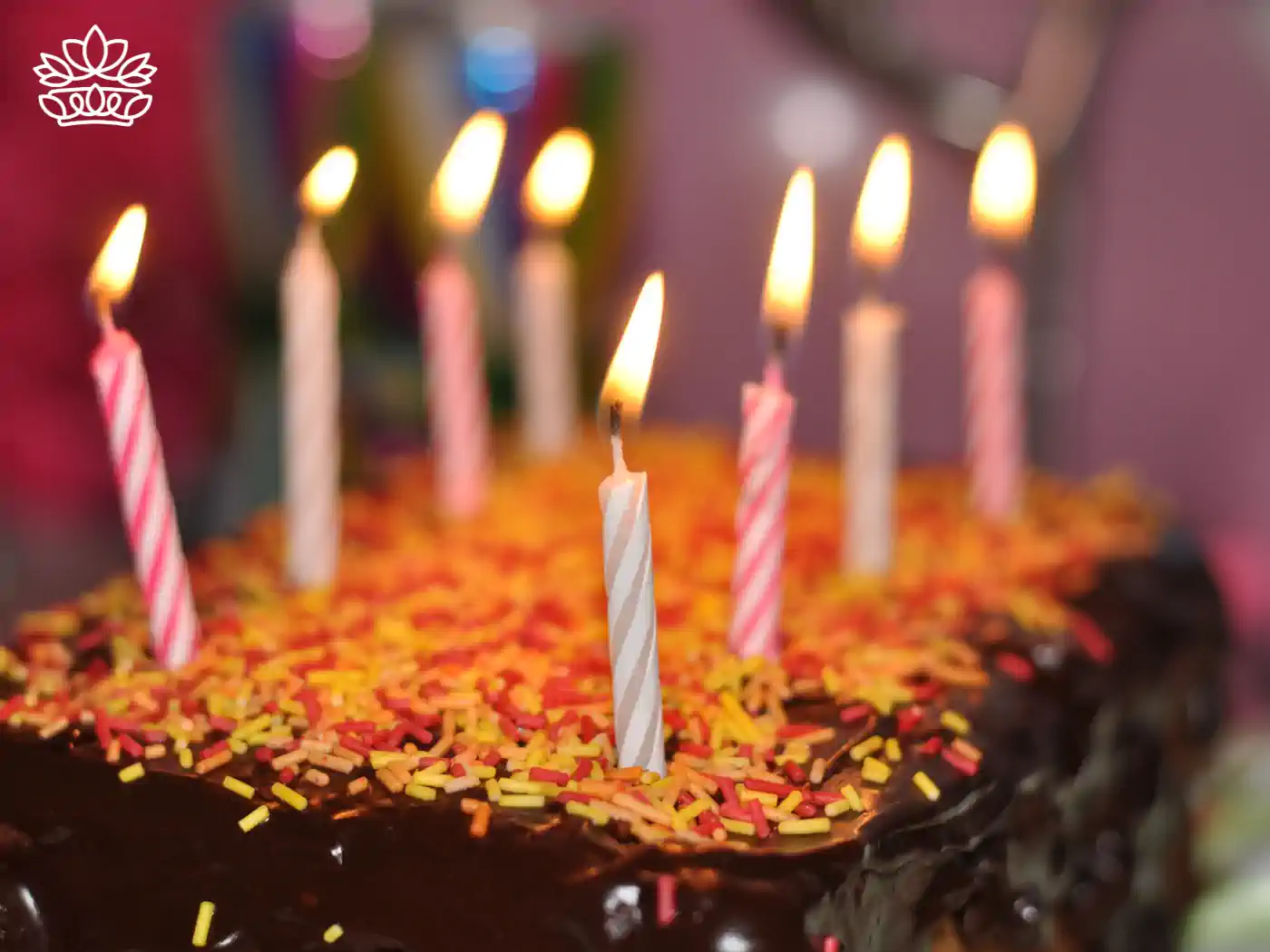 A close-up of a chocolate cake with colorful candles lit on top. Fabulous Flowers and Gifts.