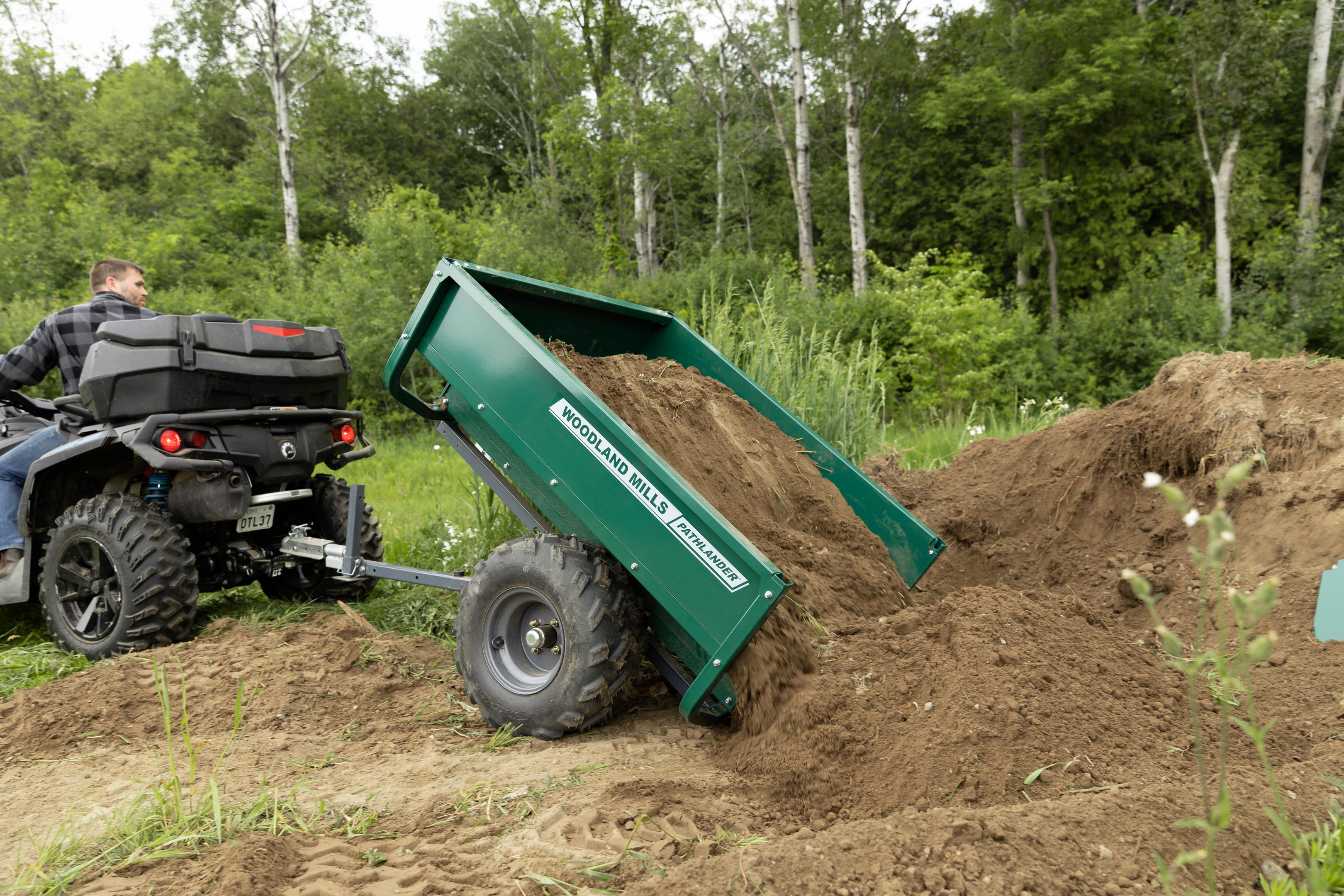 A man dumping a load of soil with a Woodland Mills Pathlander ATV Dump Trailer. 