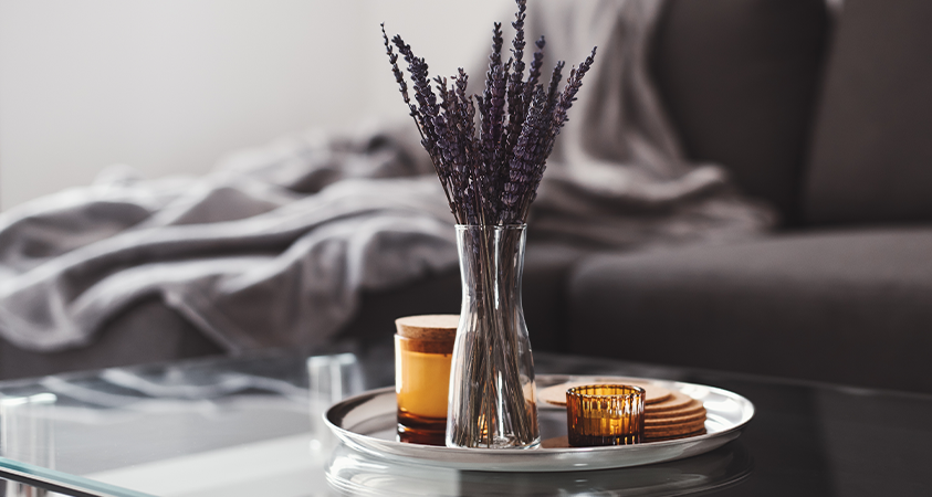 A simple glass coffee table holds a plate with a jar of lavender, a candle, a tealight and some coasters. These elements are organised to work in perfect balance.