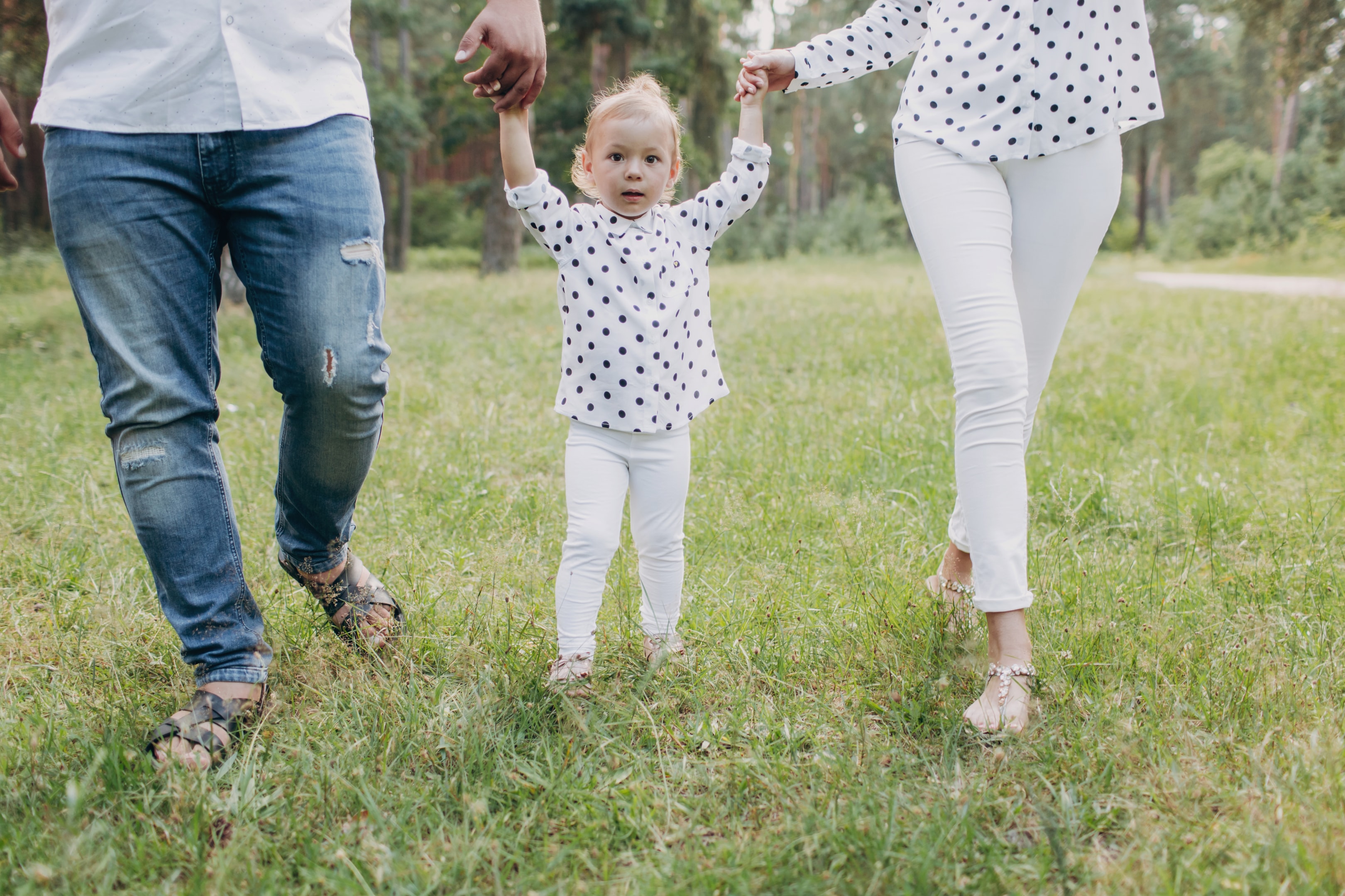 Parents holding their young child’s hands while walking together outdoors
