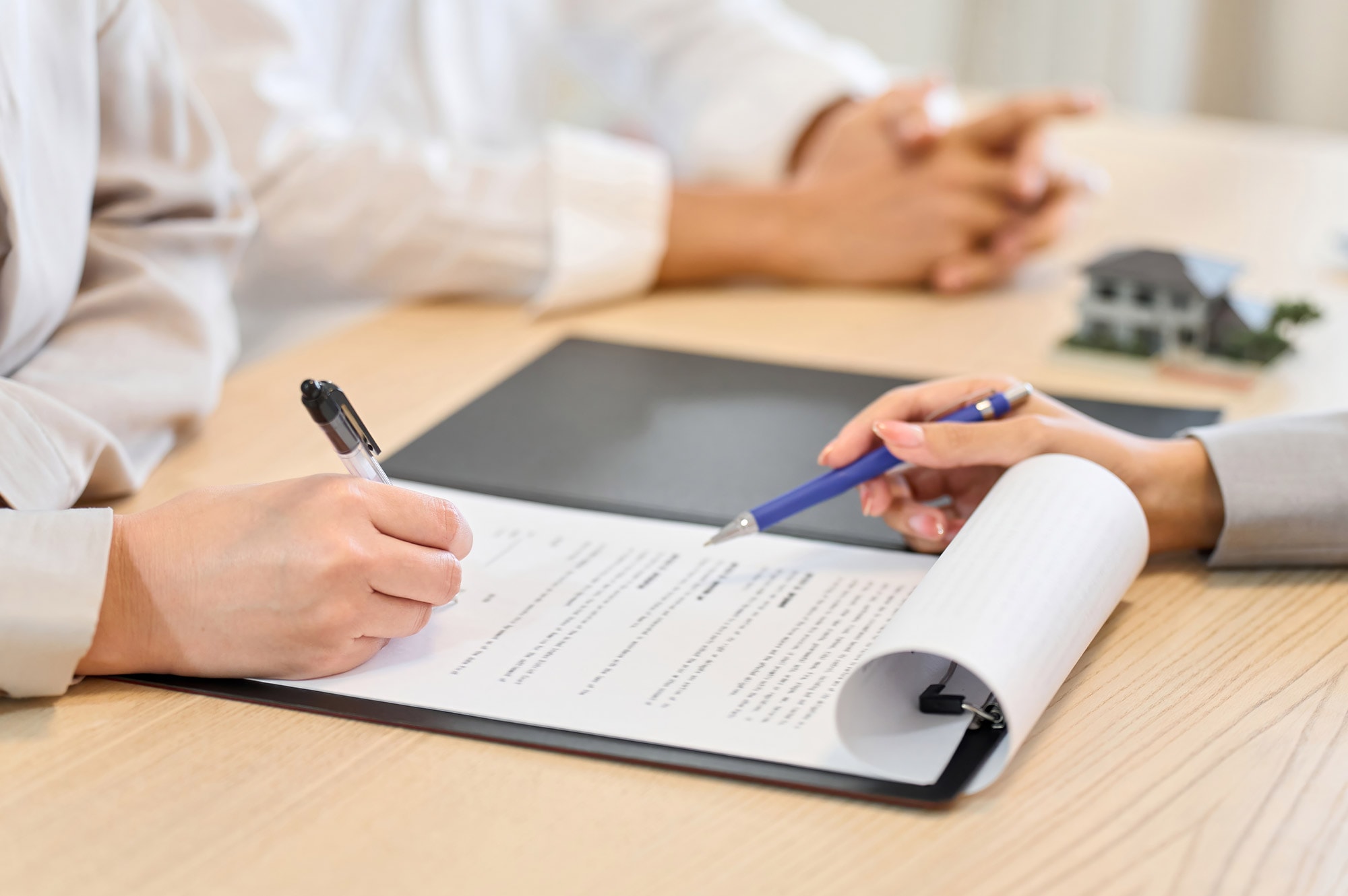 Hands signing land purchase contracts beside a model home, showcasing the application process for Land Loans in Australia.