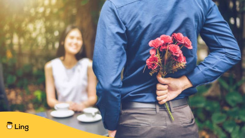 The man is hiding red flowers behind him in order to surprise his girlfriend.