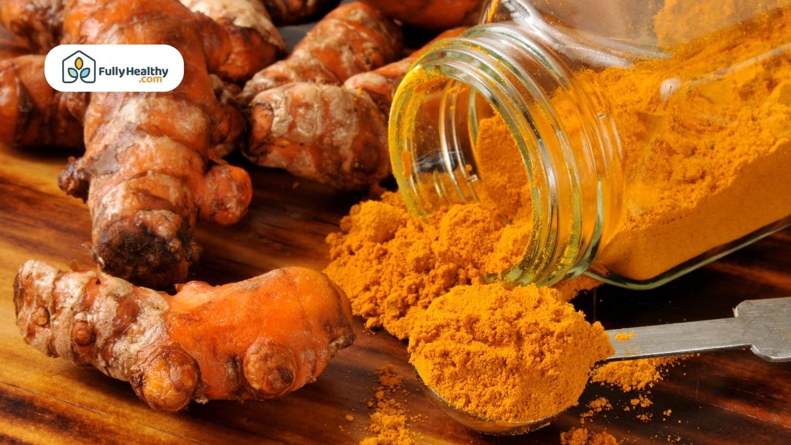 Glass jar spilling turmeric powder next to fresh turmeric roots on a wooden surface