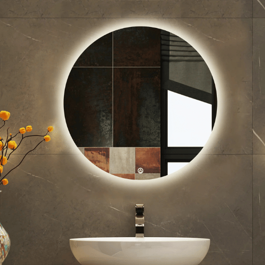 Modern bathroom setup featuring a round, backlit mirror mounted on a gray marble wall above a white vessel sink with a sleek faucet. A decorative branch with orange flowers is placed in a vase to the left of the sink.