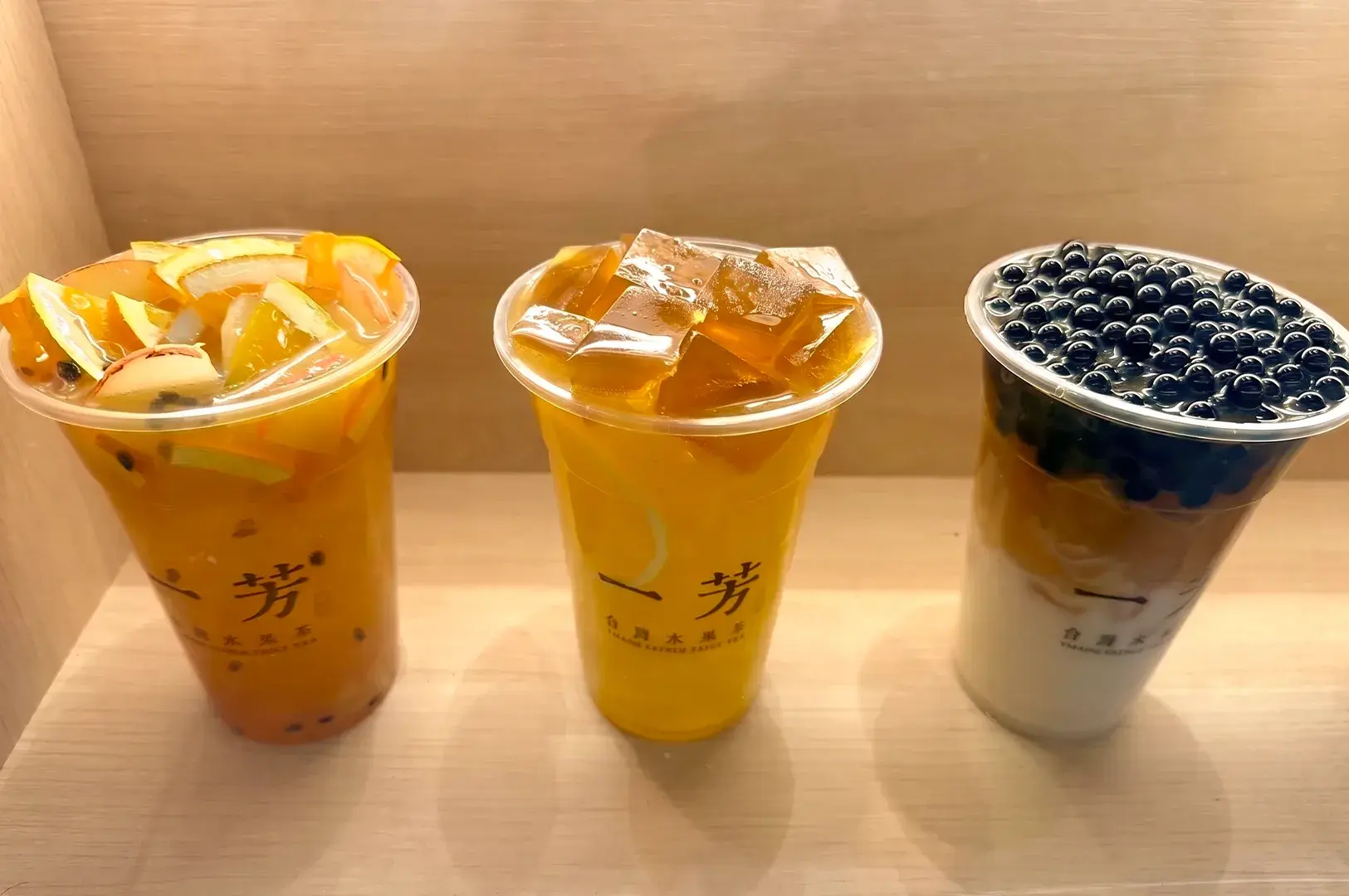 Three Yi Fang Taiwan Fruit Tea cups lined up, showcasing fruit-topped tea, jelly-topped tea, and pearl milk tea.