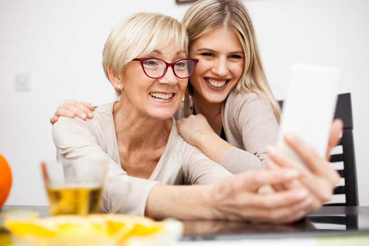 Blonde haired woman in red glasses taking a selfie with her daughter.