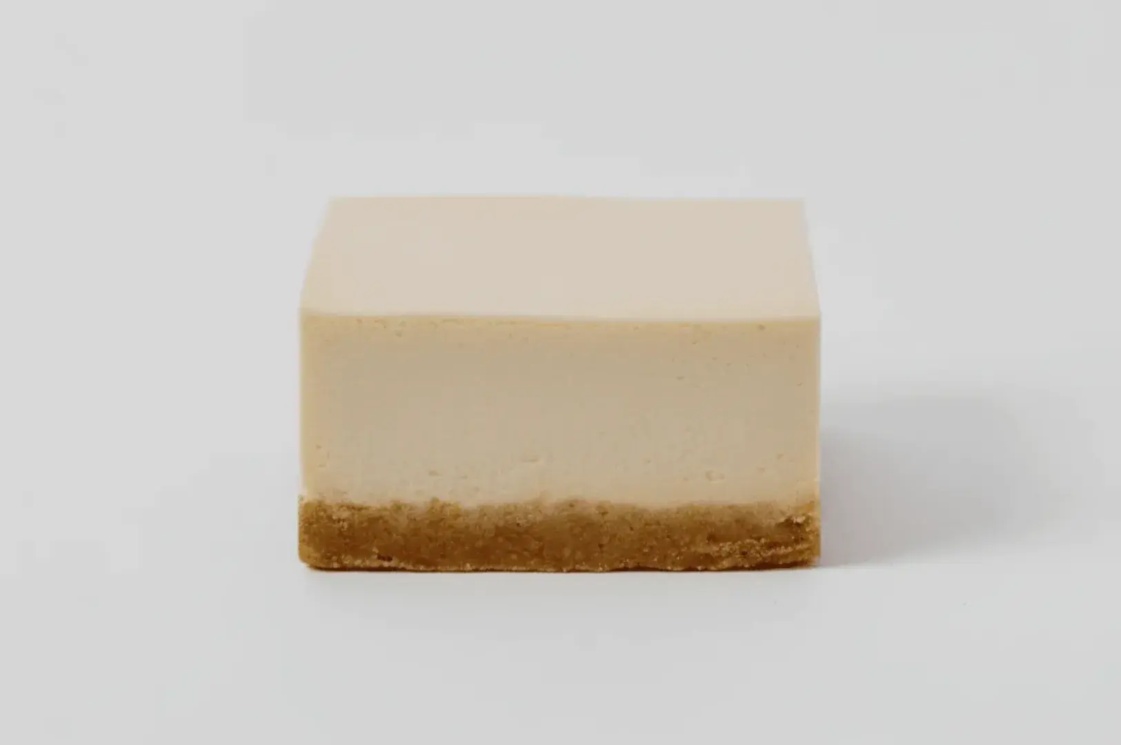 A rectangular piece of cheesecake with a smooth, creamy top layer and a crumbly base.