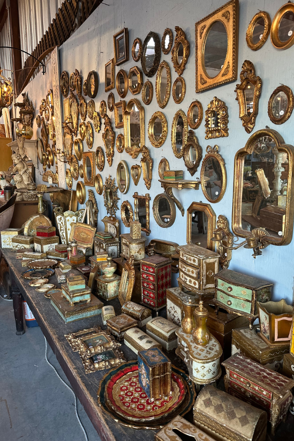 Table filled with antique decorative boxes and gilded mirrors arranged against a wall display at a Round Top antiques vendor booth.