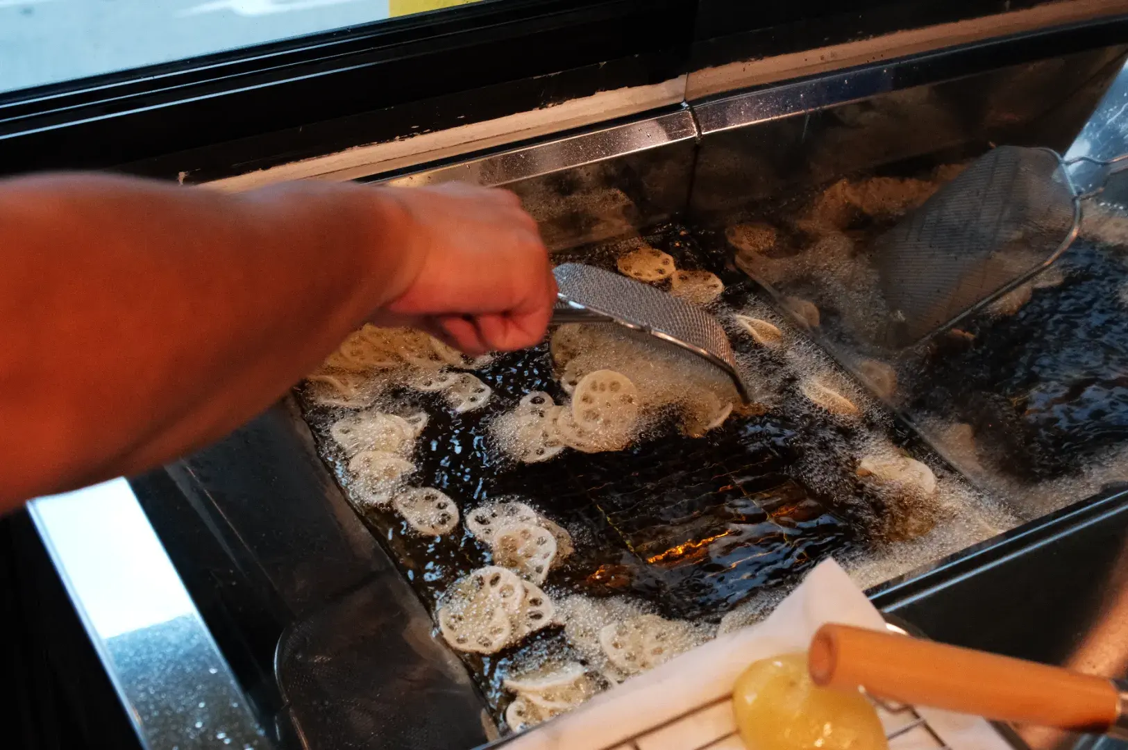 A person using a slotted spatula to fry food in hot oil, with bubbles and steam around the frying area.