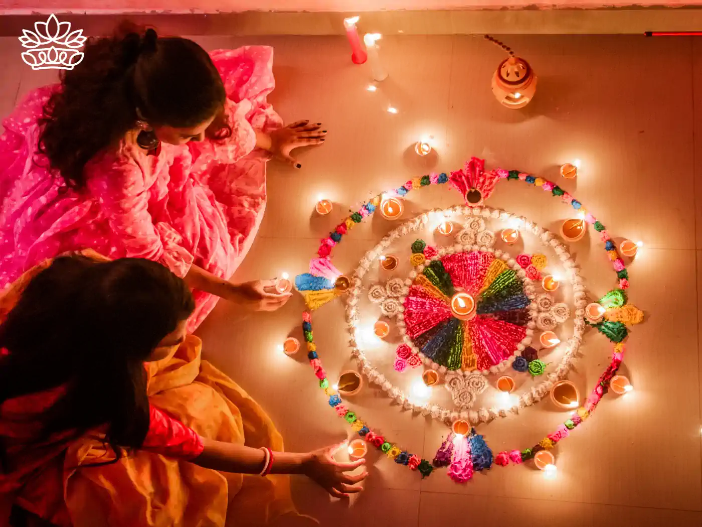 Two women in traditional attire creating a vibrant and intricate Rangoli design with candles and flower petals for Diwali celebration, evoking the festive spirit of unity and creativity. Diwali. Delivered with Heart by Fabulous Flowers and Gifts.