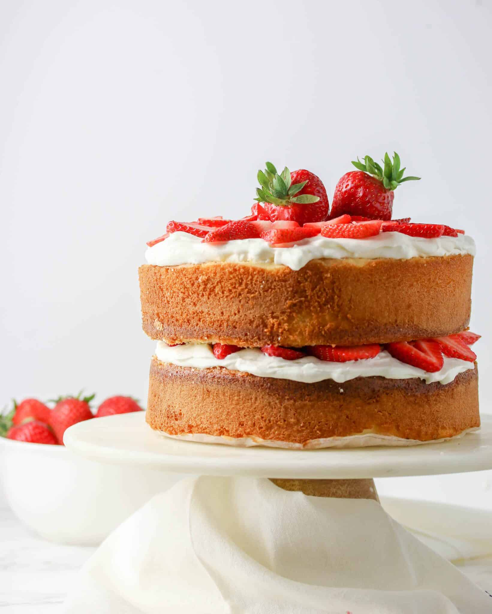 sponge cake with whipped cream and strawberries on a cake stand