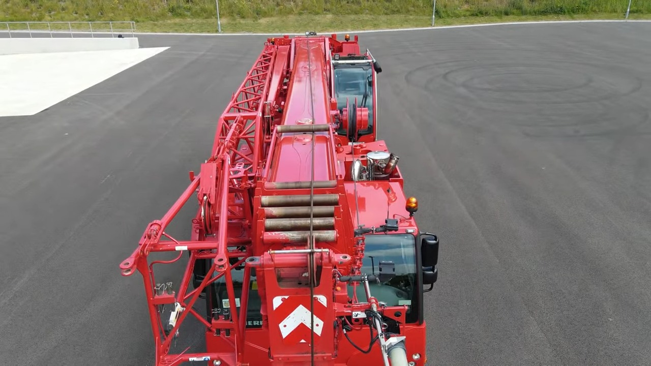 Aerial view of a large red mobile firetruck crane parked on a freshly paved road, showcasing its complex machinery and extended ladder unit for high reach operations in emergency situations