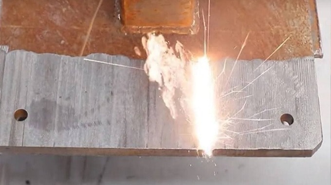 Laser beam removing rust and paint from a metal plate.