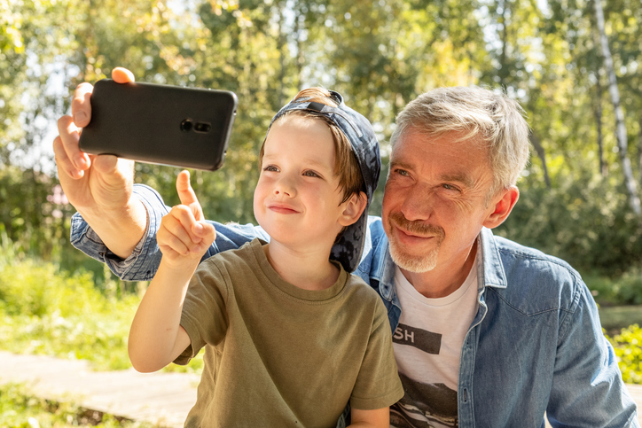 Grey-haired grandpa with his grandson smiling and looking at a cell phone.