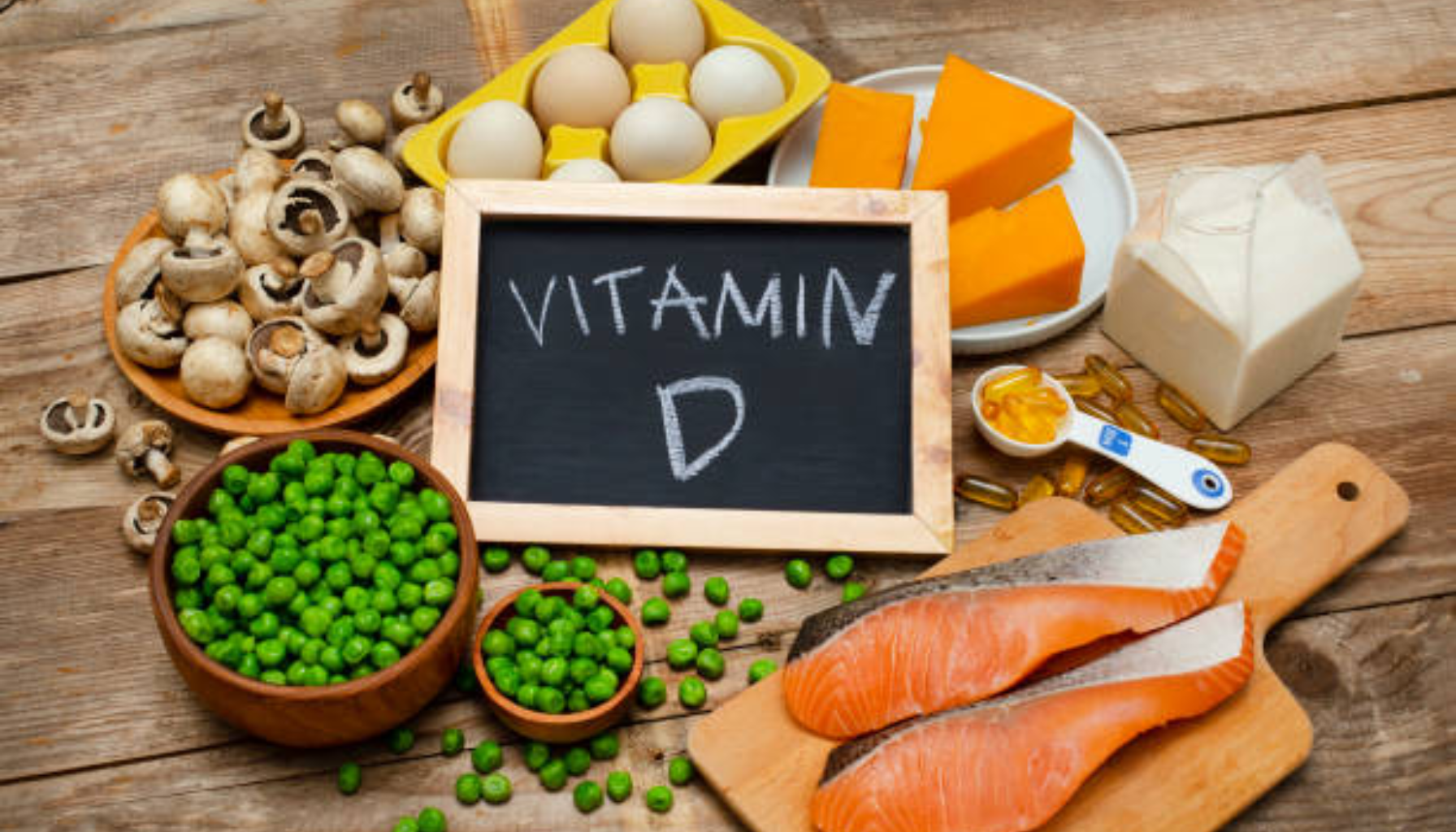 Vitamin D verdier – Hva er normalt og når bør du ta tilskudd? 18 Ulike matvarer rike på vitamin D, inkludert laks, egg, ost, sopp, erter, melk og kosttilskudd, vist på et trebord.
